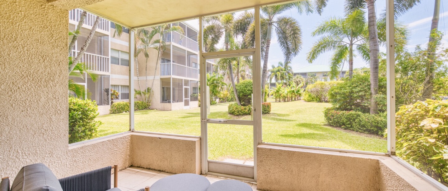 Screened lanai with cozy seating and peaceful palm-lined garden views